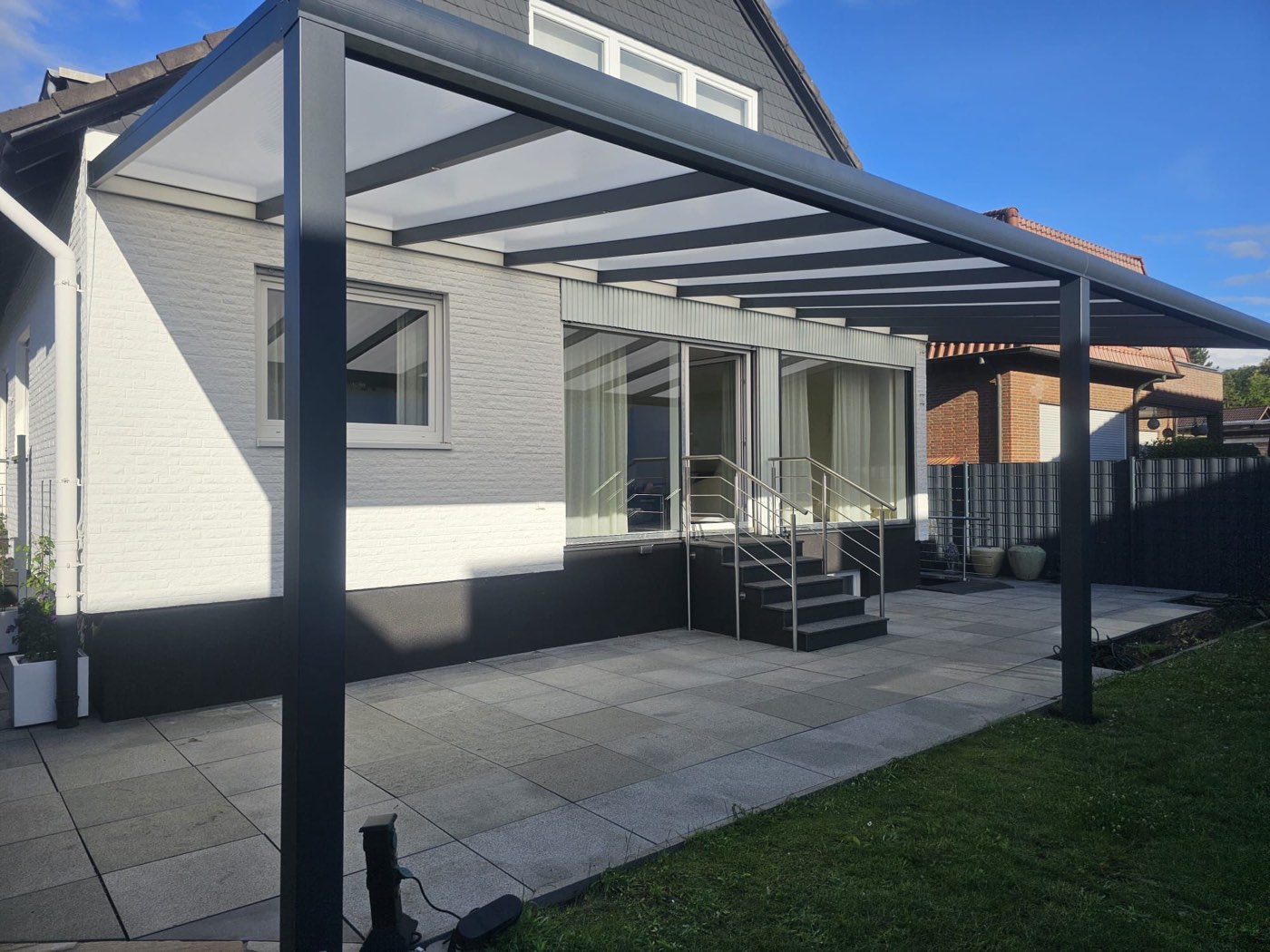 Terrassenüberdachung mit opaker Eindeckung an einem weißen Wohnhaus