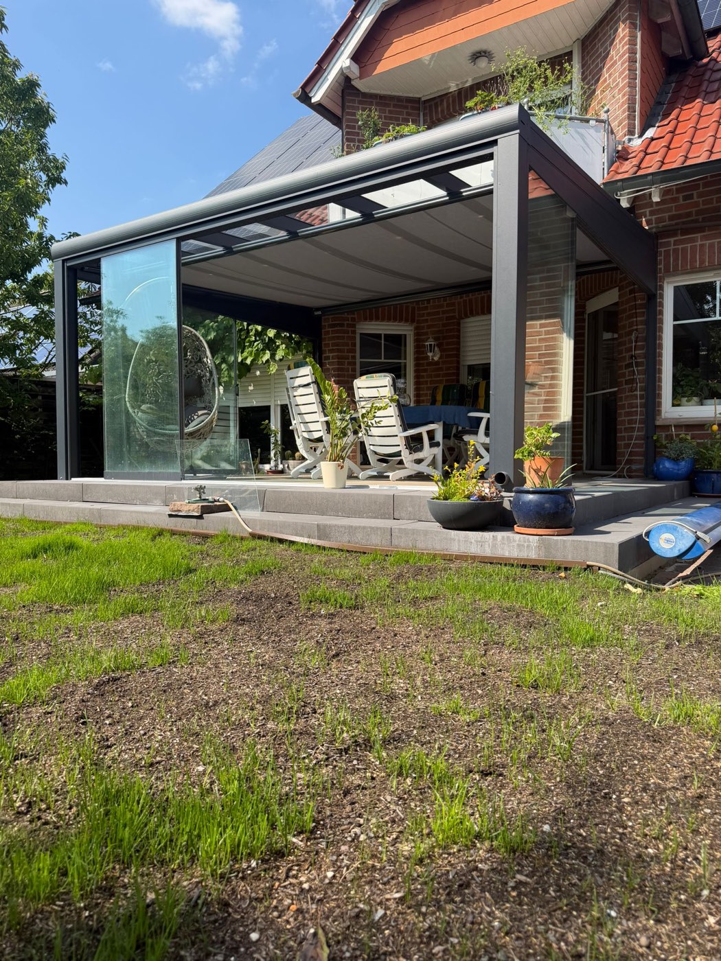 Überdachte Terrasse mit Glasschiebewänden und Bepflanzung